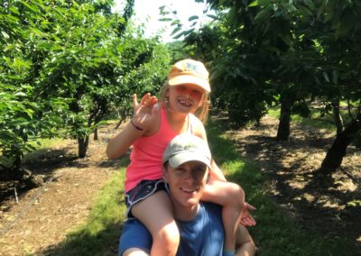 Monte Glanzer cherry picking with his daughter sitting on his shoulders.