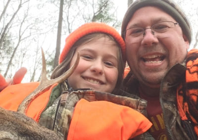 Matthew Hale and his son smiling together with a deer while hunting.