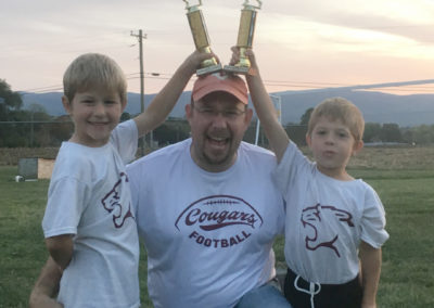 Matthew Hale and his two young sons posing together with two football trophies