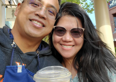 Fay Paurillo and her husband smiling together in a selfie, with a cup of iced coffee in her hand.