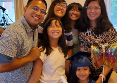 Fay Paurillo, her husband, and four young daughters smiling together at a celebration, with her youngest daughter wearing a cap and gown.
